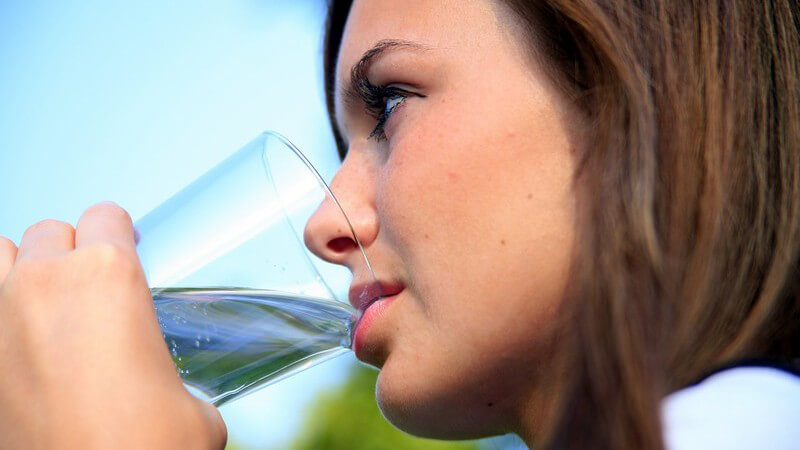 Seitenansicht junge dunkelhaarige Frau trinkt aus einem Wasserglas