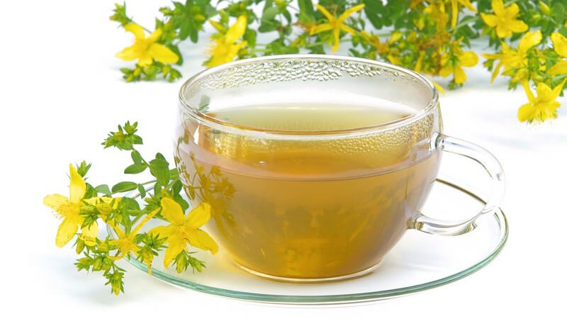 Teetasse mit Johanniskraut Tee umgeben von Johanniskrautblüten auf weißem Hintergrund