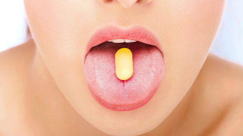 Nahaufnahme ausgestreckte Zunge einer Frau mit gelber Tablette darauf