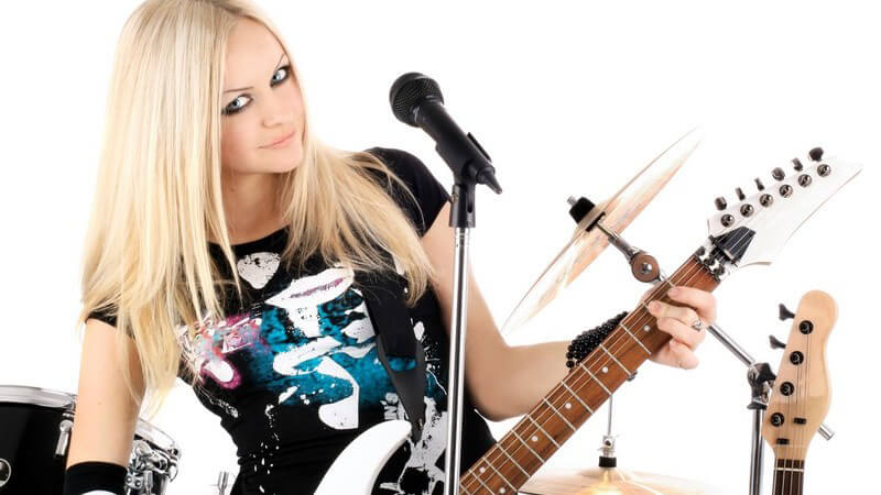 Junge blonde rockige Frau mit Gitarre steht vor Mikrofon