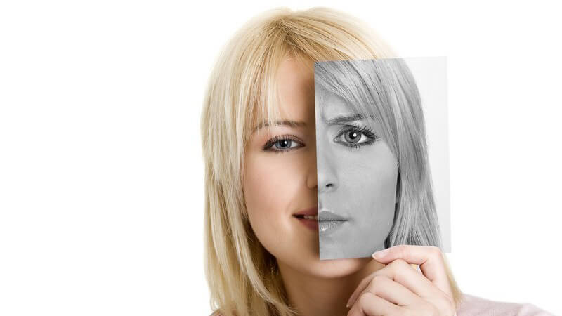 Junge Frau hält sich Foto mit ihrem Gesichtsausschnitt schwarz weiß vors Gesicht