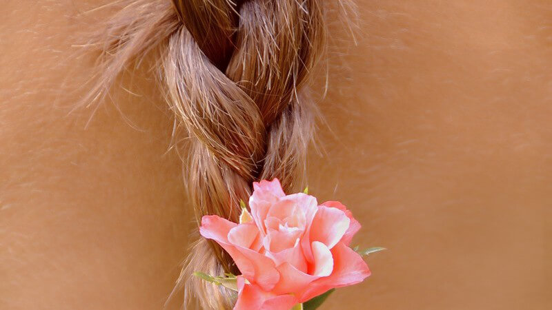 Rückansicht Ende eines blonden geflochtenen Zopfes mit Rosenblüte