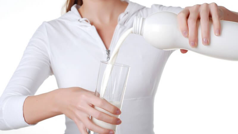 Junge Frau kippt Milch aus Plastikflasche in ein Glas, weißer Hintergrund