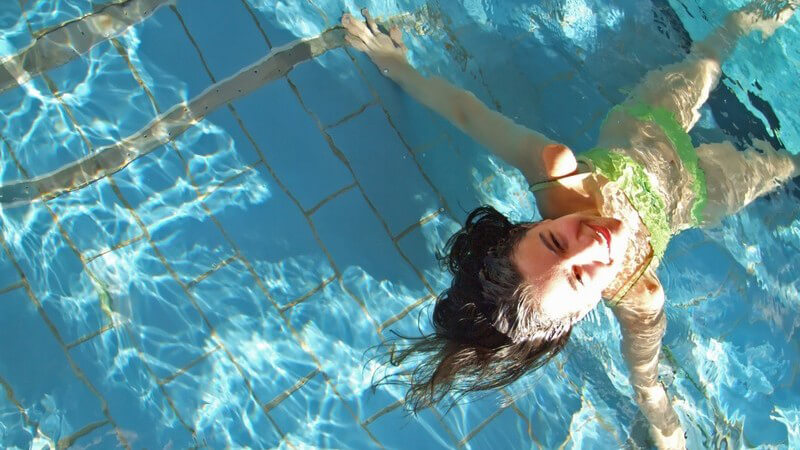 Mädchen in grünem Bikini in blauem Pool, von oben betrachtet, blickt in die Kamera