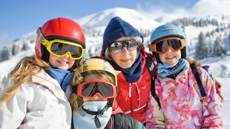 Mutter mit drei Kindern im Skirulaub mit Helmen und Skibrillen