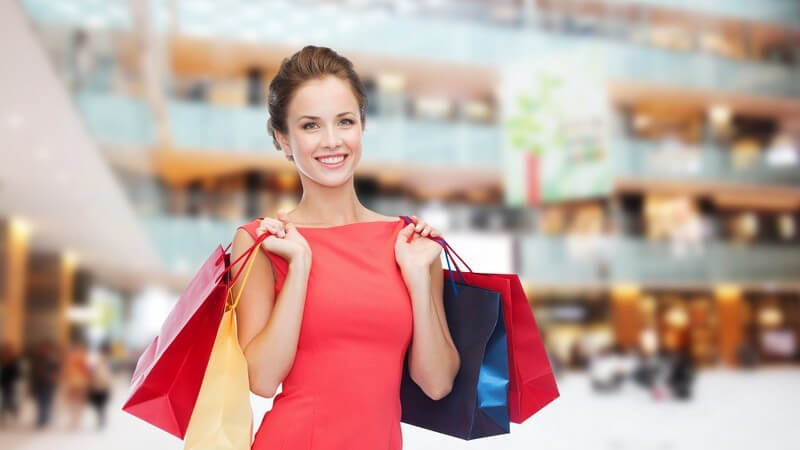 Frau beim Shopping mit Einkaufstüten in großem Einkaufszentrum
