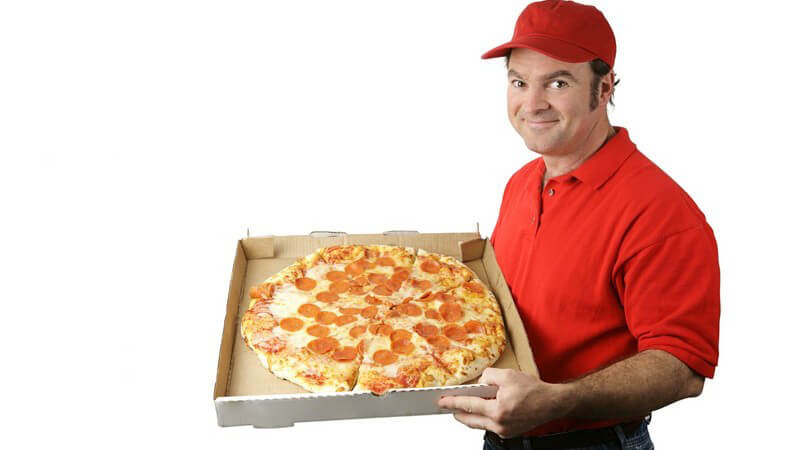 Pizzabote in rotem Shirt und mit roter Kappe präsentiert große Salami Pizza