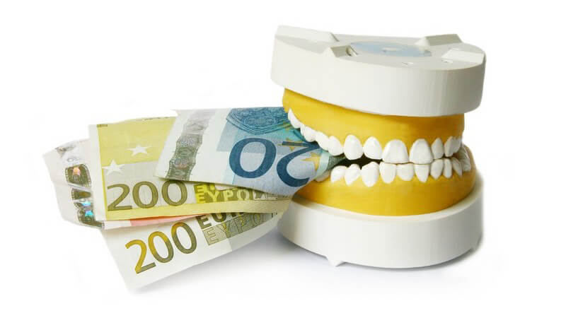 Zahnmodell beißt auf Geldscheine, weißer Hintergrund