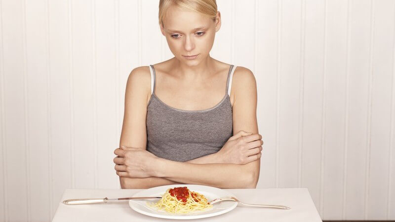 Dünnes Mädchen sitzt mit verschränkten Armen am Tisch, vor ihr ein Teller mit Spaghetti