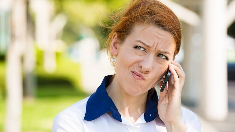 Frau steht draußen und telefoniert mit ihrem Handy, hat einen skeptischen Blick