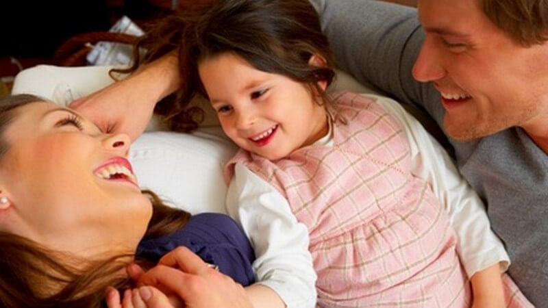 Lachende, fröhliche Familie mit kleiner Tochter auf dem Sofa, sich gegenseitig zugewendet