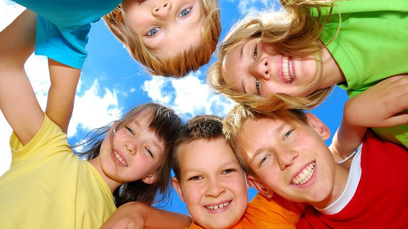 Ansicht von unten: fünf Kinder stehen im Kreis und lächeln in Kamera