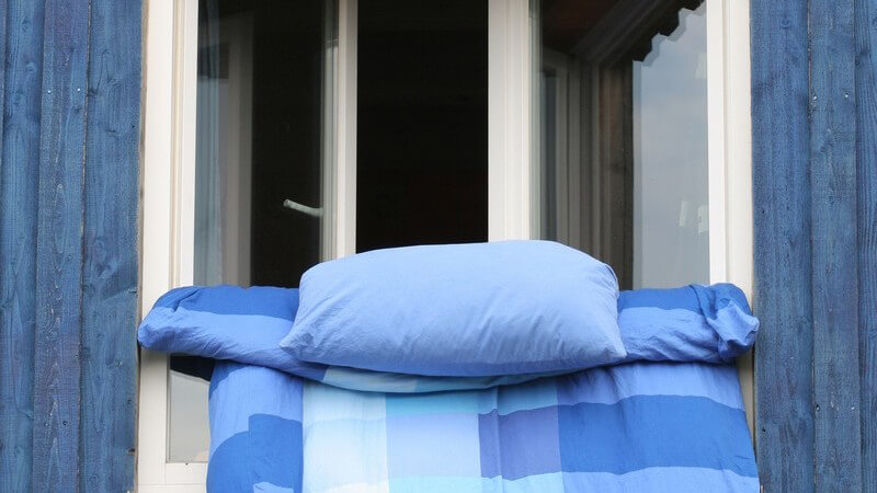 Bettwäsche hängt zum Lüften aus Fenster eines blauen Hauses