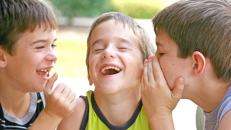 Kleine lachende Jungen sagen sich etwas ins Ohr