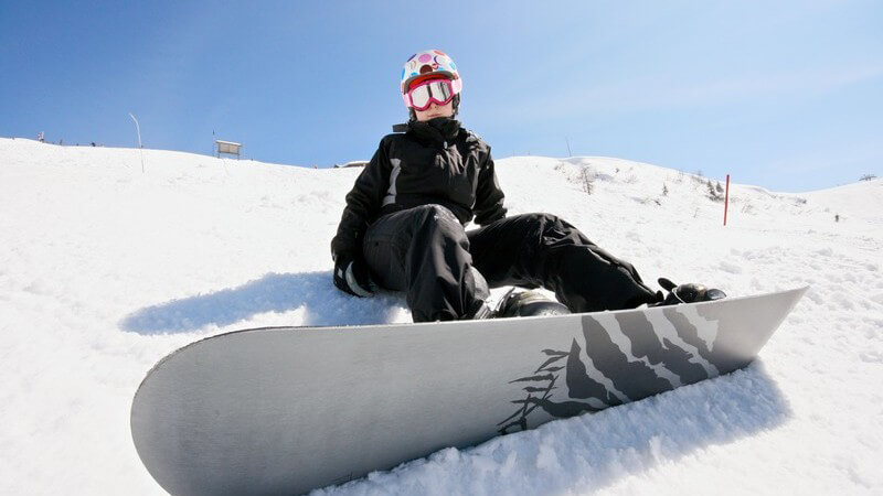 Snowboarder sitzt auf Skipiste unter blauem Himmel
