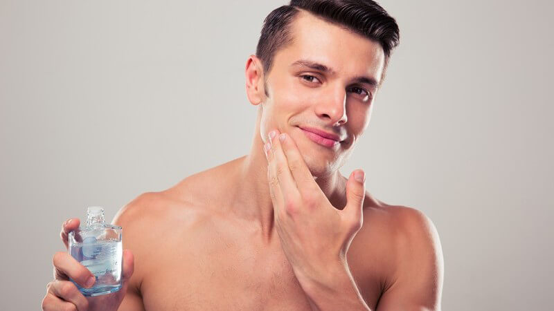 Gepflegter Mann mit kurzen braunen Haaren reibt sein Gesicht mit Aftershave ein