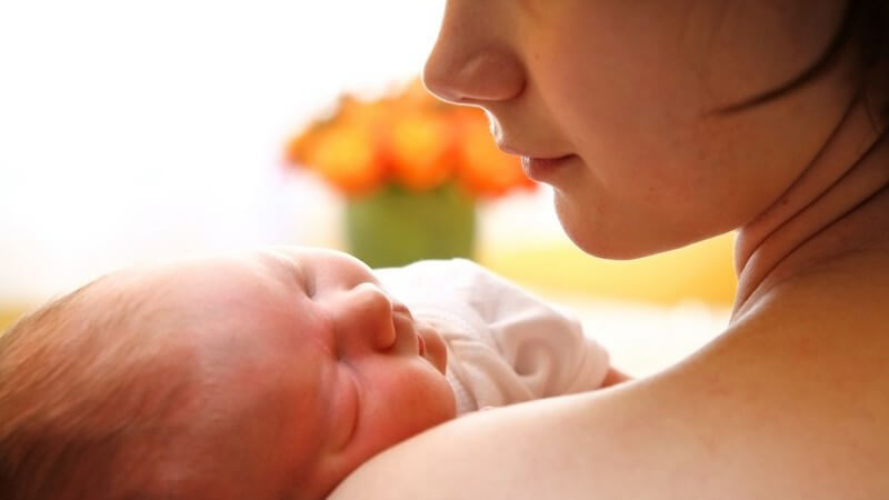 Rückenansicht junge Mutter hält Neugeborenes im Arm und schaut es an