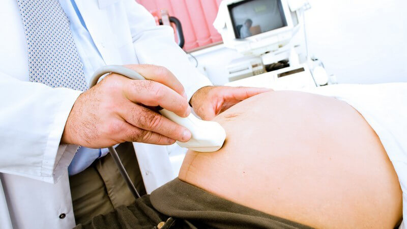 Hand eines Frauenarztes mit Ultraschallgerät macht Ultraschallbild von Baby im Bauch einer Frau