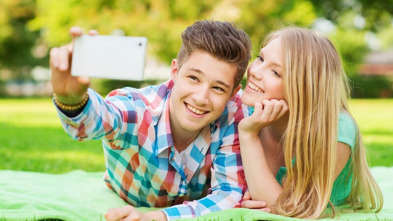 Selfie: junges Paar liegt im Park auf einer Wiese und macht ein Foto mit dem Handy
