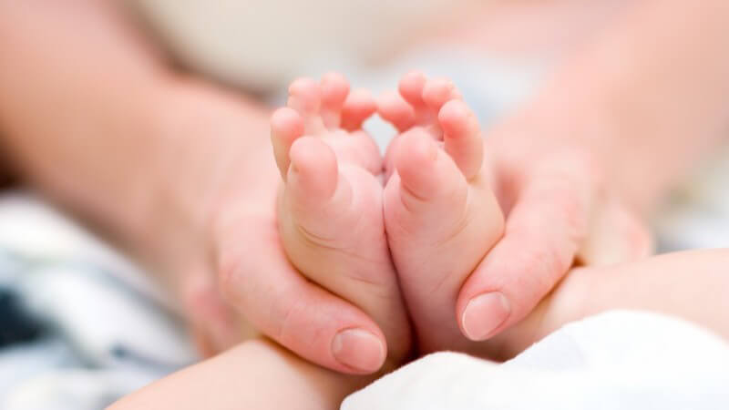 Hände der Mutter halten Babyfüßchen fest