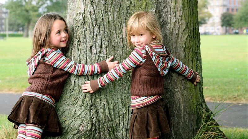 Zwei kleine Schwestern umarmen Baum