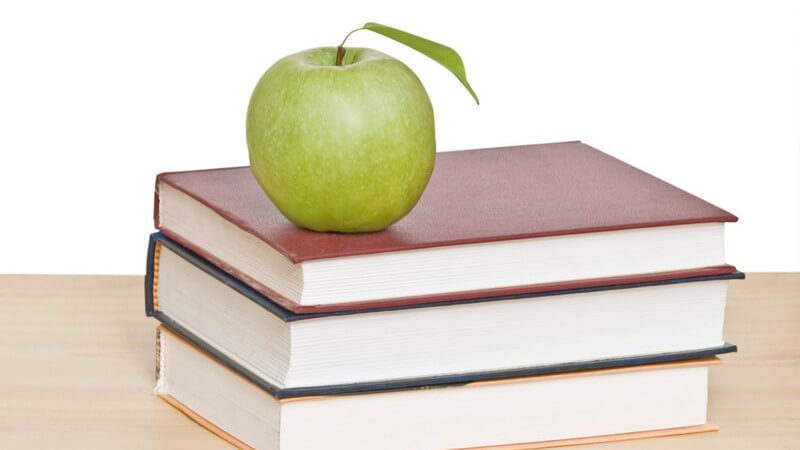 Grüner Apfel auf Stapel Bücher, davor Bleistift