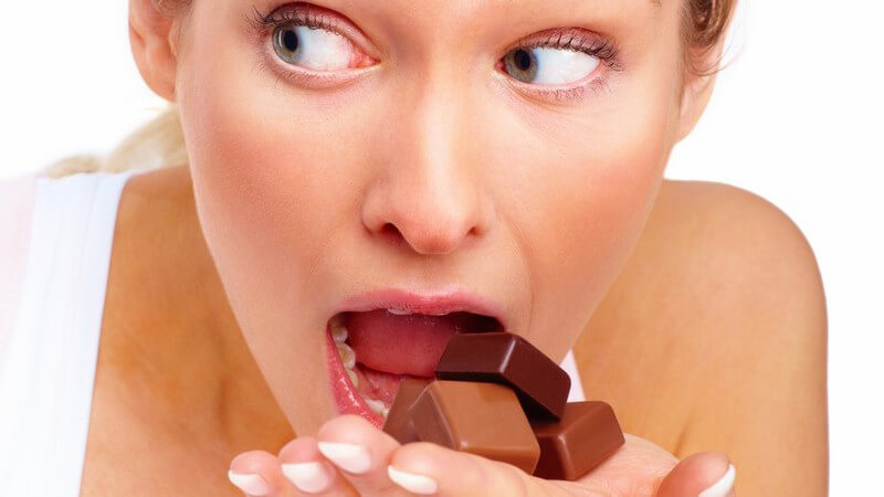 Blonde Frau isst heimlich Schokoladen Pralinen