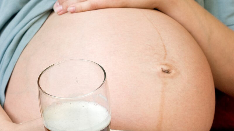 Nahaufnahme Babybauch, Schwangere hält Glas Bier in der Hand