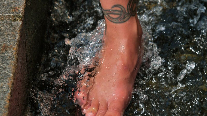 Weiblicher Fuß mit im Wasserbad umgeben von Stein, Tattoo am Fußgelenk