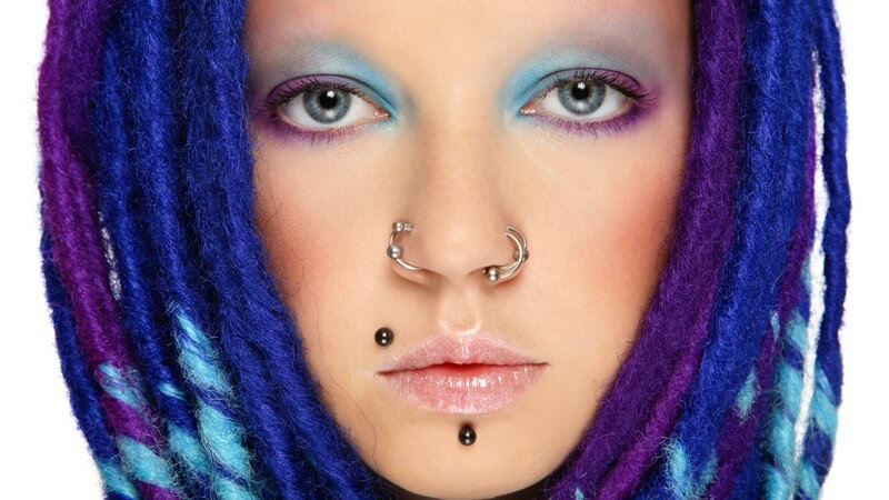 Gesichtsportrait junge Frau mit mehreren Piercings und blauen Dreads