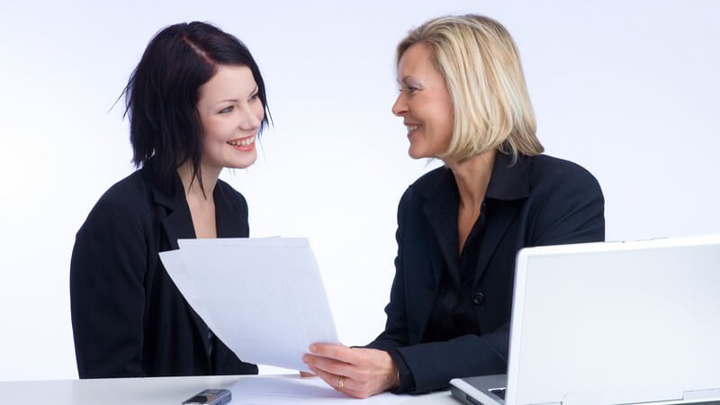 Beruf - Chefin mit weißem Laptop und Papieren im Gespräch mit einer Angestellten