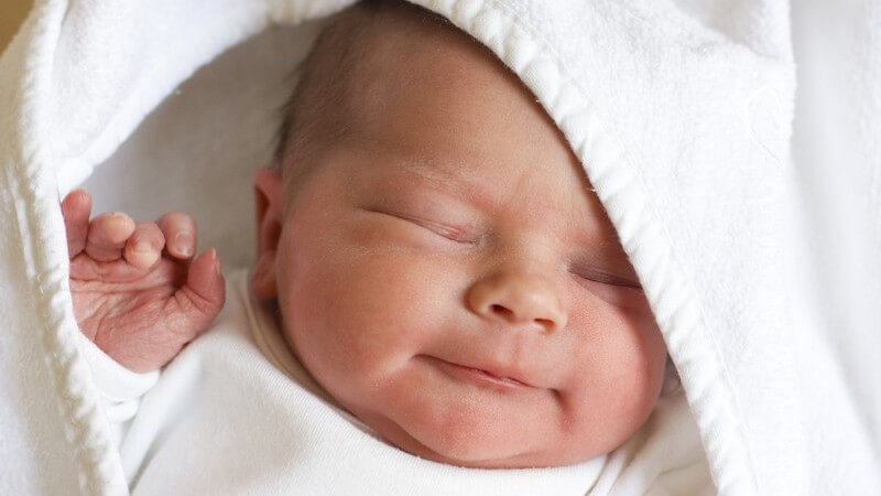 Oberkörper eines neugeborenen schlafenden Babys in weißer Kleidung