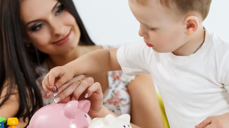 Mutter und Sohn stecken Geldmünzen in ein rosa Sparschwein