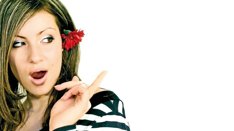 Junge Frau mit roter Blume im Haar schaut nach hinten, widerspricht mit offenem Mund und erhobenem Finger