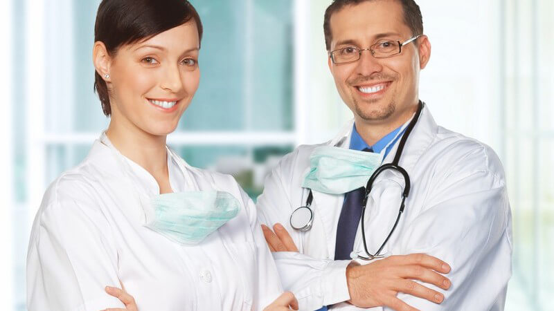 Portrait eines Arztes mit seiner Helferin, beide in weißen Kitteln, lächelnd
