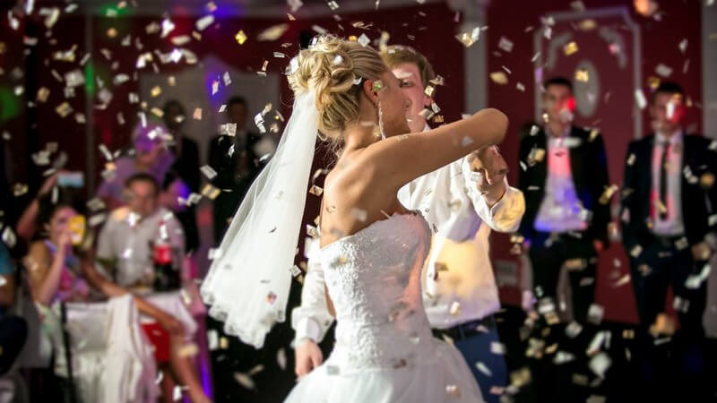 Blonde Braut mit Schleier beim Hochzeitstanz in glitzerndem Konfettiregen