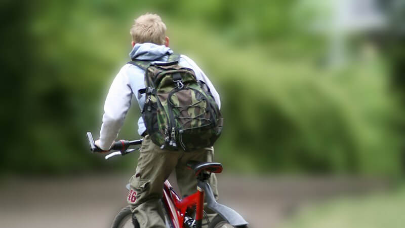 Rückansicht Junge mit Rucksack auf Fahrrad