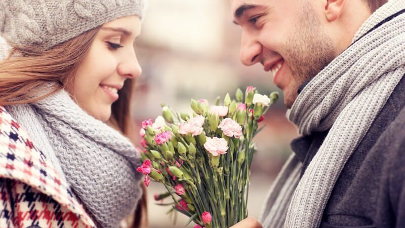 Junges Paar in Wintermode steht sich gegenüber, er hat ihr gerade Blumen geschenkt