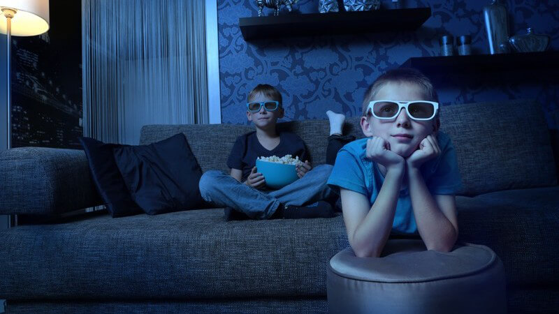 Zwei Jungen sitzen in einem dunklen Raum und gucken einen Film mit 3-D-Brillen