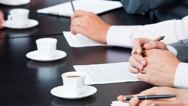 Ausschnitt Tisch, Kaffeetassen, Hände von Geschäftsleuten mit Papier und Stift bei Meeting