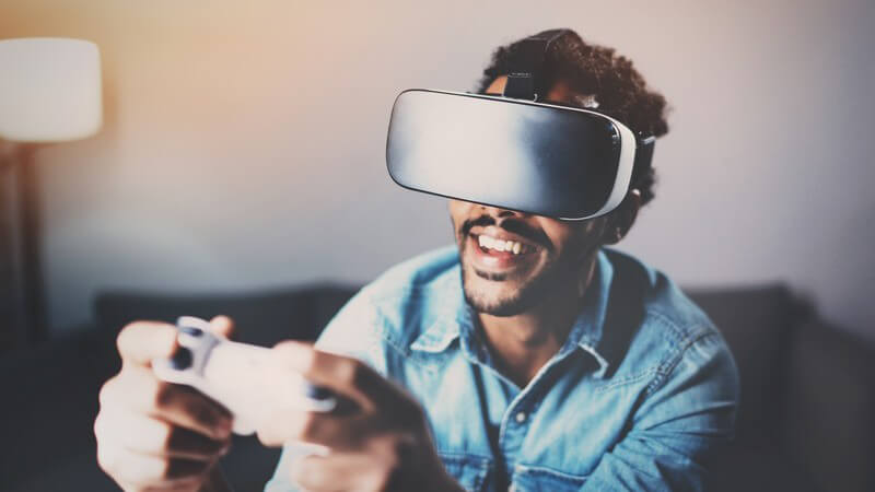 Dunkelhäutiger Mann beim Videospielen mit Spielkonsole und VR-Brille