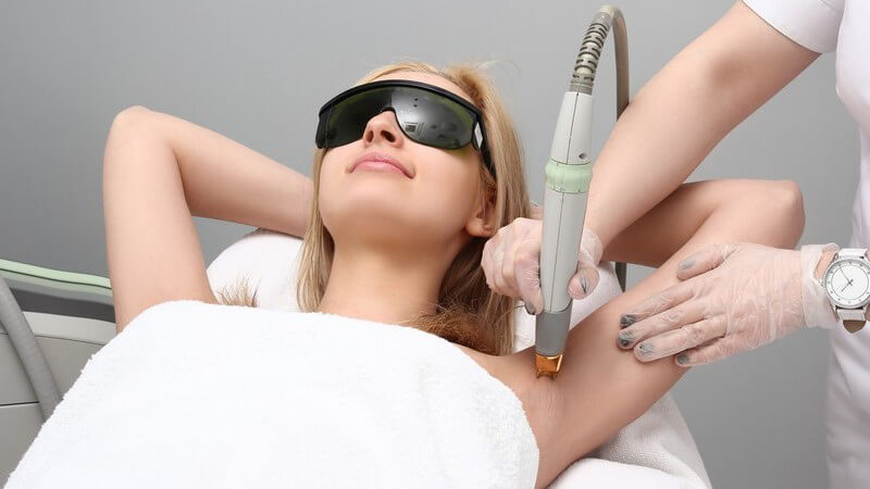 Frau mit Schutzbrille bekommt eine Laserbehandlung unter den Achseln zur dauerhaften Haarentfernung