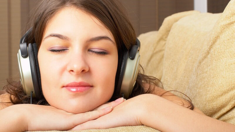 Junge, dunkelhaarige Frau mit geschlossenen Augen hört Musik über Kopfhörer