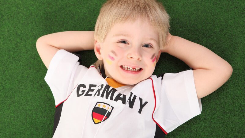 Kleiner Junge mit Fußballtrikot liet auf Rasen, Deutschlandfan
