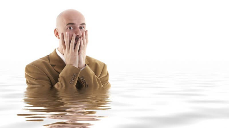 Mann im Anzug steht fast bis Schultern im Wasser, Hände erschrocken vor dem Gesicht
