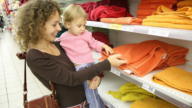 Junge Mutter mit Baby auf Arm beim Einkaufen, Regal mit Handtüchern