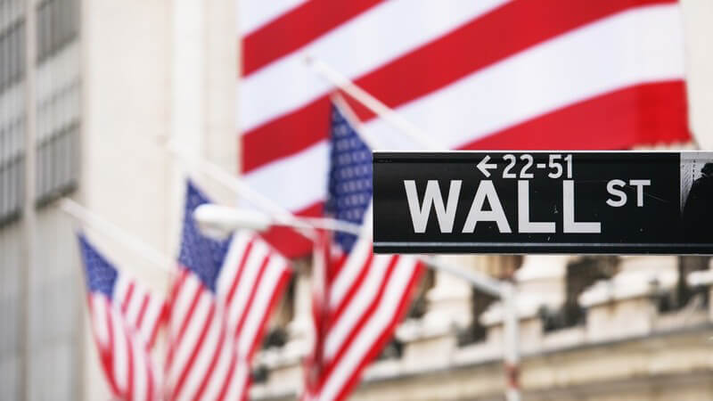 Straßenschild der Wall Street in New York vor der Börse mit US-Flaggen