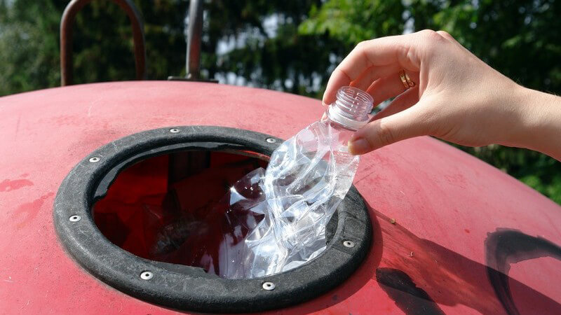 Rechte Frauenhand wirft Plastikflasche in Mülltonne