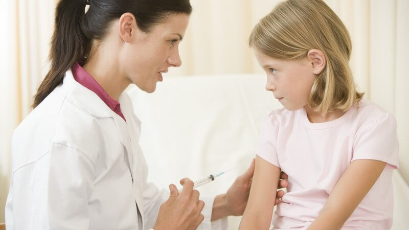Junge Ärztin mit Mädchen im Behandlungsraum, beruhigt Patientin vor der Spritze