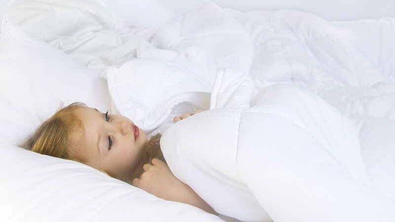 Kleines Mädchen unter weißer Bettdecke auf dem Rücken liegend im Bett